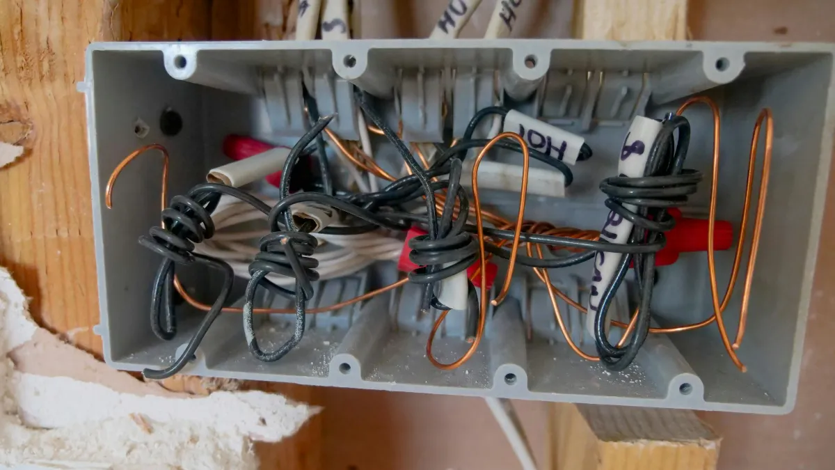 Electrician working at a consumer unit with mobile phone showing Voco AI receptionist notification nearby